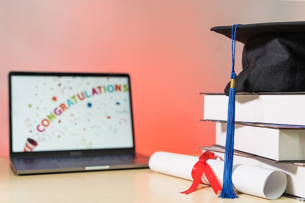 Tapa de graduación con libros y certificado de diploma aislado en mesa de madera