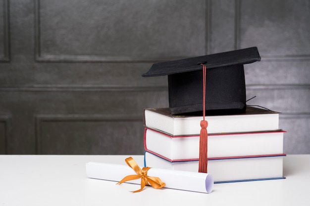 Tapa de graduación con libros sobre escritorio blanco, fondo de educación