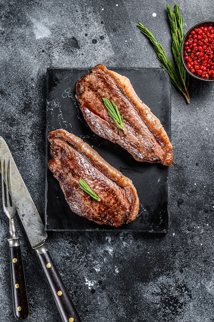 Tapa de solomillo a la parrilla o bistec picanha sobre una tabla de cortar de piedra. Fondo negro. Vista superior.