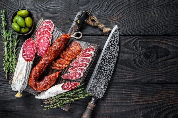 Tapas espanholas fatiadas salame de salsichas, fuet e chouriço em uma tábua de madeira. fundo de madeira preto. vista do topo. copie o espaço.