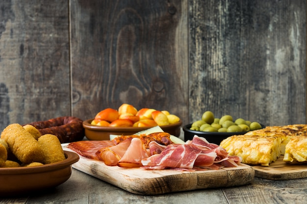 Tapas espanholas tradicionais. Croquetes, azeitonas, omelete, presunto e patatas bravas na mesa de madeira