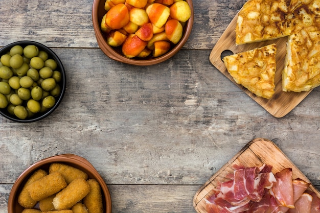 Tapas espanholas tradicionais. Croquetes, azeitonas, omelete, presunto e patatas bravas na mesa de madeira