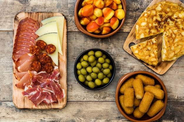 Tapas espanholas tradicionais Croquetes, azeitonas, omelete, presunto e patatas bravas na mesa de madeira