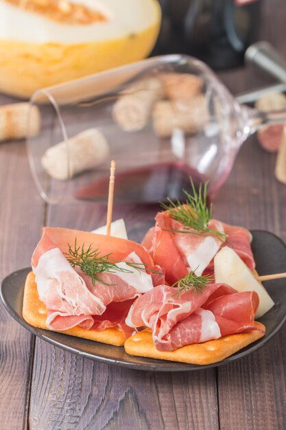 tapas españolas rebanadas de jamón de carne de cerdo curado con melón y vino tinto sobre fondo de madera