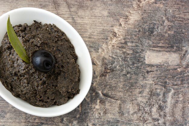 Tapenade de aceituna negra con anchoas, ajo y aceite de oliva en mesa de madera