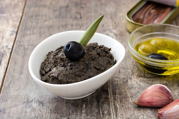 Tapenade aus schwarzen Oliven mit Sardellen, Knoblauch und Olivenöl auf Holztisch