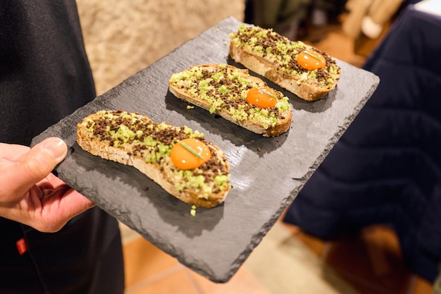 Tapenade von Sardellen und Couscous auf Toast auf einem schwarzen Tablett-Stillleben