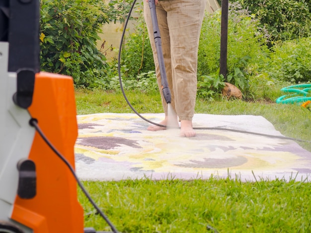 Tapete lavável à pressão. Limpando carpetes com spray profissional de extração, menina lava carpetes na rua