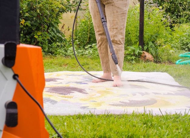 Tapete lavável à pressão. Limpando carpetes com spray profissional de extração, menina lava carpetes na rua