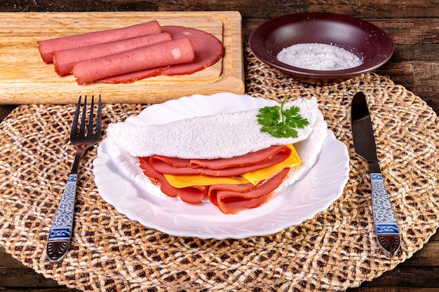 Tapioca beiju com presunto, queijo e mortadela no prato sobre a mesa.