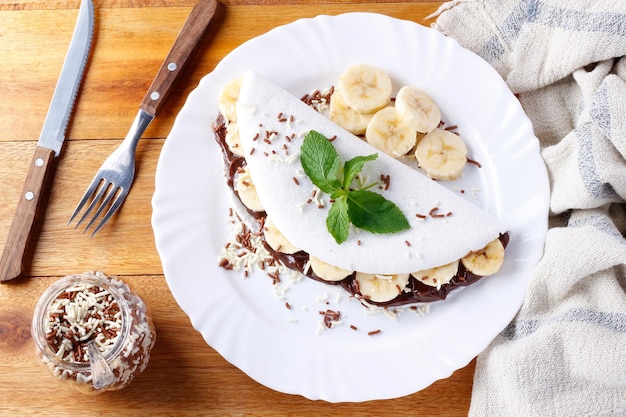 Tapioca caseira ou beiju recheado com banana e chocolate na chapa branca sobre mesa de madeira rústica