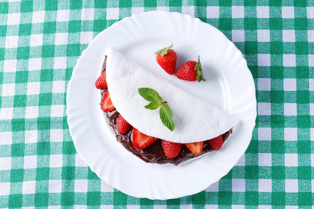 Foto tapioca casera o beiju rellena de fresa y chocolate en un plato blanco sobre una mesa rústica de madera