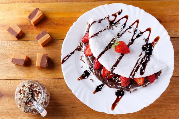 Tapioca casera o beiju rellena de fresa y chocolate en un plato blanco sobre una mesa rústica de madera