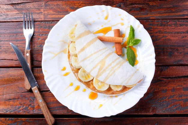 Tapioca casera o beiju rellena de plátano y leche condensada o caramelo malteado sobre mesa rústica de madera