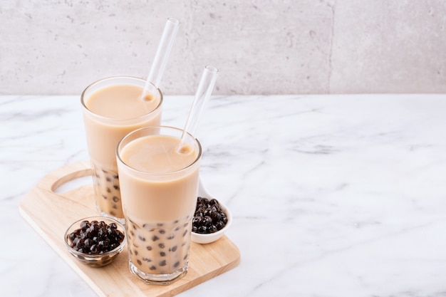 Tapioca pearl ball bubble milk tea, bebida popular de Taiwán, en vaso con paja sobre mesa de mármol blanco y bandeja de madera, de cerca, copie el espacio.