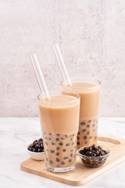 Tapioca pearl ball bubble milk tea, bebida popular de Taiwán, en vaso con paja sobre mesa de mármol blanco y bandeja de madera, de cerca, copie el espacio.