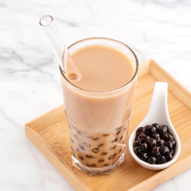 Tapioca pearl ball bubble milk tea, bebida popular de Taiwán, en vaso con pajita sobre mesa de mármol blanco y bandeja de madera