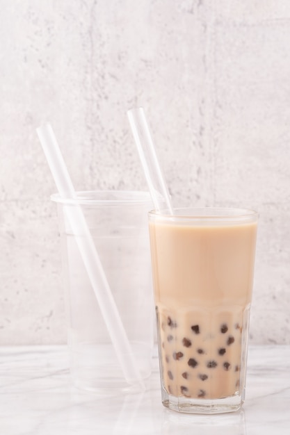 Tapioca pearl ball bubble milk tea, bebida popular de Taiwán, en vaso con pajita sobre mesa de mármol blanco y bandeja de madera