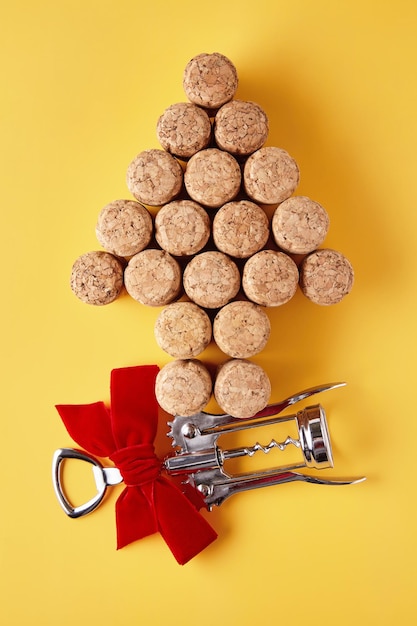 Foto los tapones de champán dispuestos en forma de árbol de navidad y un sacacorchos de metal atado con una cinta sobre un fondo amarillo