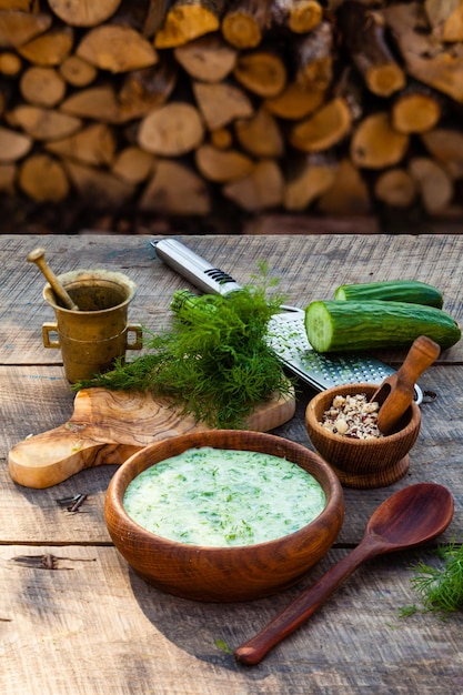 Tarator frío casero con ingredientes sobre fondo rústico de madera. Sopa fría tradicional búlgara de verano con pepinos, eneldo, ajo, yogur y nueces.