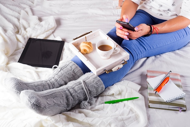 Tarde acogedora, calcetines de lana cálidos, manta suave, velas. Mujer relajante en casa, beber cacao, usando la computadora portátil. Cómodo estilo de vida.