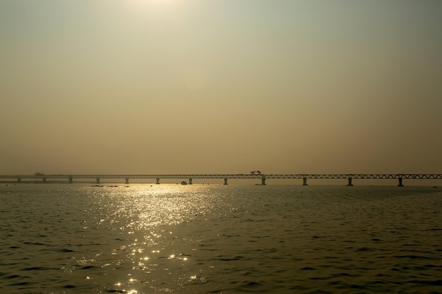 En la tarde nublada se puede ver el Puente Multipropósito PADMA en construcción en el río Padma El reflejo de la luz del sol brilla en el agua del río