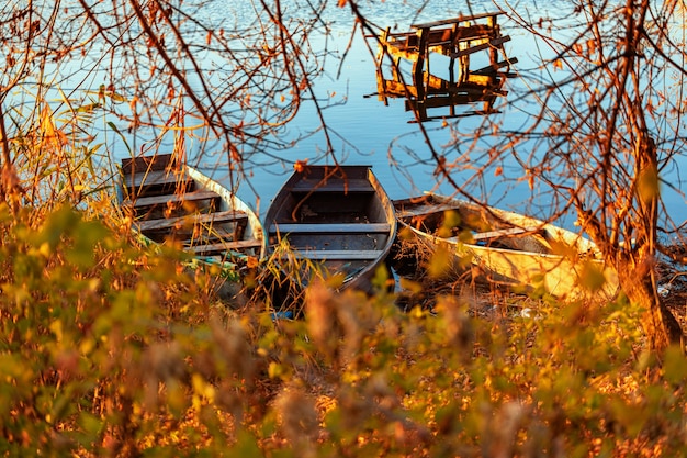 Tarde de otoño en la orilla de un río desierto con un viejo puente pesquero y tres barcos de pesca nadie