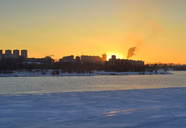 Tarde en el río Ob Siluetas de casas al atardecer en la orilla congelada de un gran río