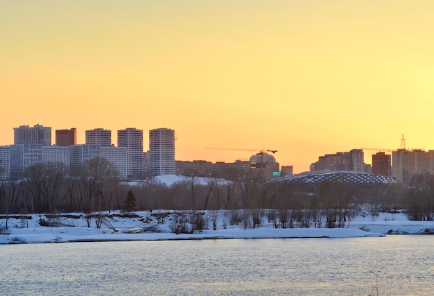 Tarde en el río Ob Siluetas de casas al atardecer en la orilla congelada de un gran río