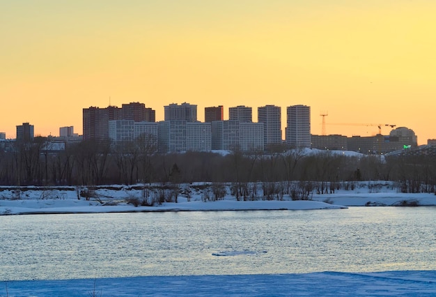 Tarde en el río Ob Siluetas de casas al atardecer en la orilla congelada de un gran río