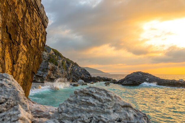 Tarde de verano y una pequeña playa en una playa rocosa. Ola rompe en rocas costeras con muchas salpicaduras