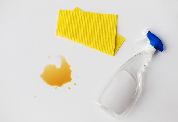 tareas domésticas, limpieza y concepto doméstico - trapo de limpieza, spray detergente y mancha derramada sobre fondo blanco