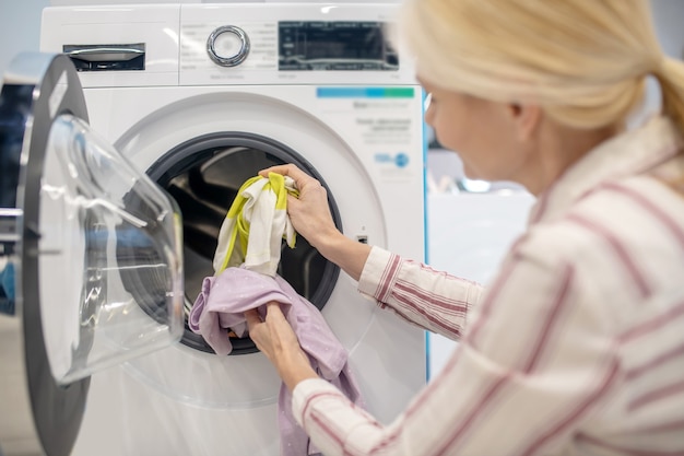 Tarefas domésticas. Dona de casa colocando roupas na máquina de lavar