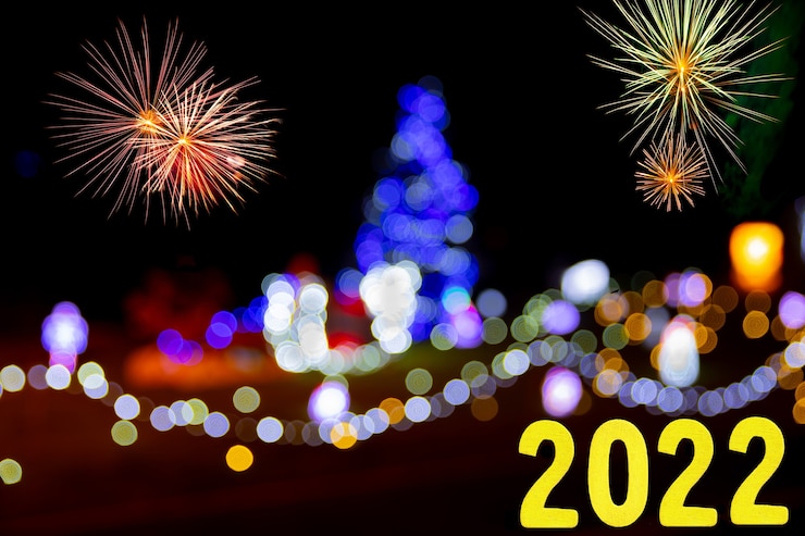 Foto tarjeta de año nuevo para 2022 con números de oro sobre un fondo de fuegos artificiales y luces de colores.