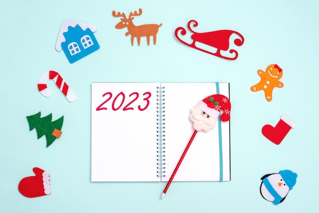 Tarjeta de Año Nuevo 2023 Pluma de cuaderno abierta vacía con Santa Claus y juguetes de Navidad sobre fondo azul