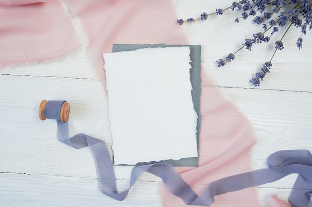 Tarjeta en blanco blanca sobre un fondo de tela rosa y azul con flores de lavanda