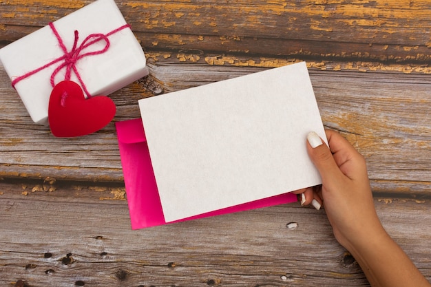 Tarjeta en blanco celebrada por mano femenina sobre fondo decorado para el día de San Valentín.