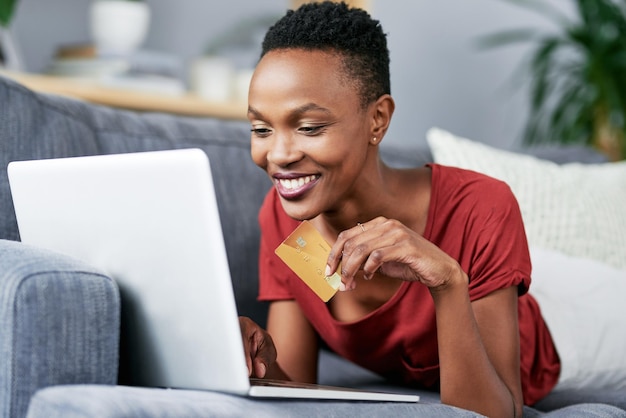 La tarjeta de crédito de la computadora portátil y la mujer negra se relajan en un sofá para comprar en línea, comercio electrónico y membresía Puntaje de crédito bancario y mujer africana feliz con la reserva de pago o la experiencia del cliente