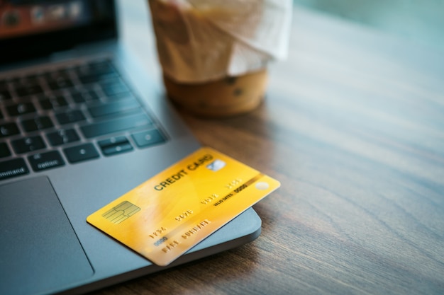 Tarjeta de crédito de la computadora portátil y la taza de café en la mesa de madera de en el fondo del espacio de copia de la cafetería, concepto de banca en línea