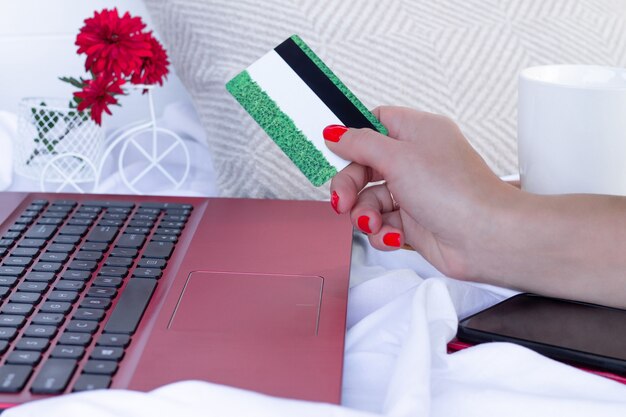 Tarjeta de crédito en mano cerca del teclado de un portátil rojo