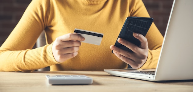 Tarjeta de crédito de mano de mujer y teléfono con computadora en la mesa