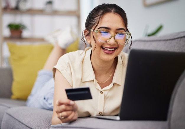 Tarjeta de crédito de mujer feliz y dinero con computadora portátil en el sofá para pago de comercio electrónico contraseña fintech y compras en línea Computadora de cliente femenino y código bancario para promoción de ventas financieras en casa