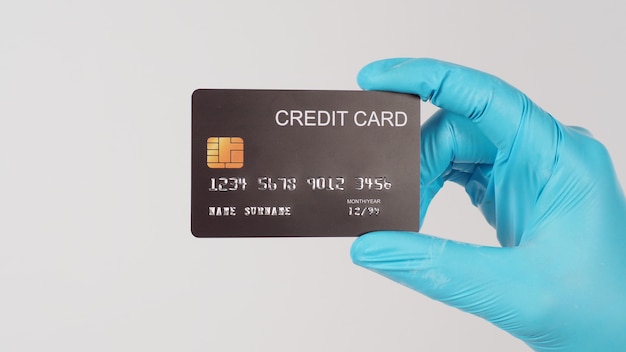 Tarjeta de crédito negra en mano con guante médico azul sobre fondo blanco tiro lateral.