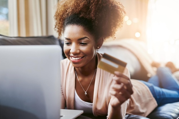 Tarjeta de crédito portátil y mujer negra en el sofá para compras en línea compra de internet y pago en el hogar comercio electrónico fintech y persona feliz en la computadora para compras ventas de sitios web y banca digital