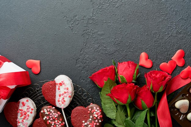 Tarjeta del día de San Valentín Rosa flores rojas galletas de brownie y dulces de chocolate en caja de regalo en forma de corazón con vino sobre fondo negro Tarjeta de felicitación del Día de la Madre o de la Mujer Vista superior plana