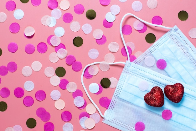 Tarjeta para el día de san valentín. sobre un fondo rosa máscaras médicas y dos corazones rojos. felicitaciones divertidas. Vista plana endecha, superior.