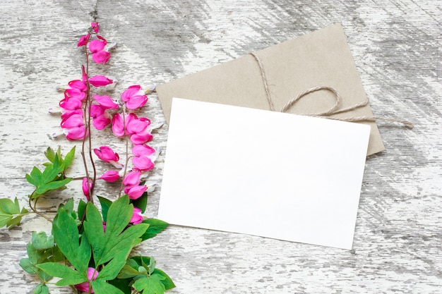Tarjeta de felicitación blanca en blanco y sobre con ramo de flores silvestres rosas