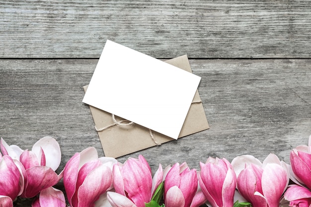 Tarjeta de felicitación en blanco con flores de magnolia rosa sobre mesa de madera rústica. aplanada vista superior