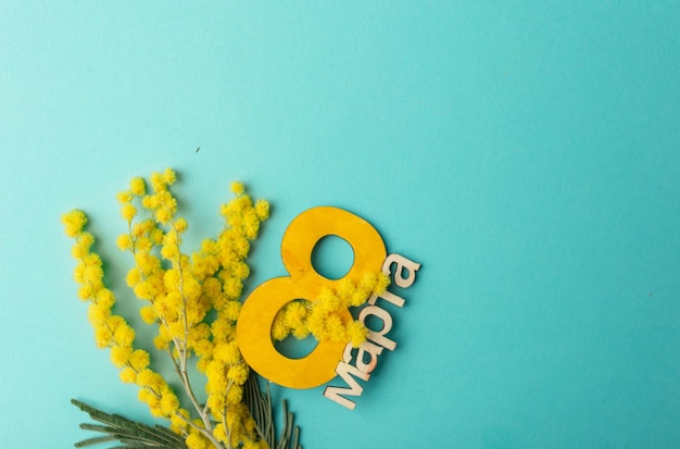 Tarjeta de felicitación para el Día Internacional de la Mujer 8 de marzo Fondo azul con un ramo de flores de mimosa y el número ocho de madera