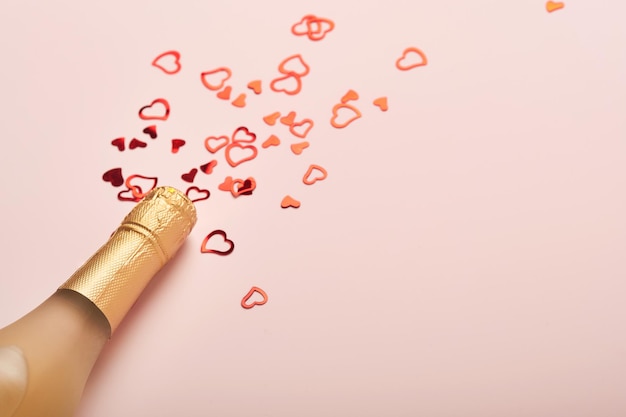 Tarjeta de felicitación del día de San Valentín con botella de champán, copas de remolque, corazones de chocolate y caja de regalo sobre fondo rosa. Vista superior con espacio para saludos. Tarjeta de felicitación con espacio de copia.